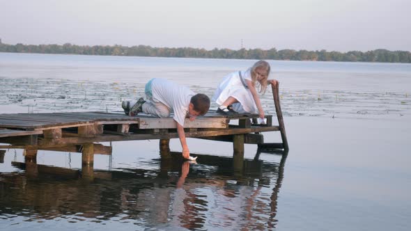 Outdoor Recreation, Cute Children Boy and Girl on Wooden Bridge Are Letting on Water River Paper