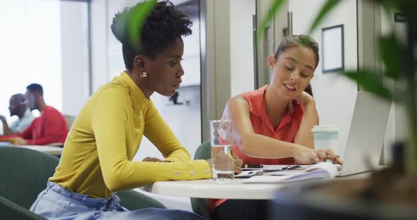 Diverse female business colleagues talking and using laptop in office