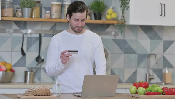 Young Man Making Online Payment on Laptop in Kitchen