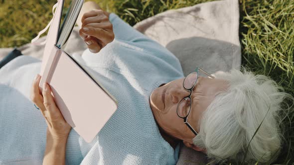 Senior Gray Haired Woman Reading a Book While Resting on the Grass in Nature