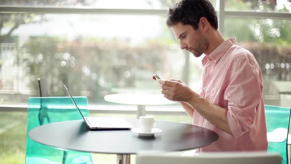 Man using laptop computer and talking on cell phone in cafe