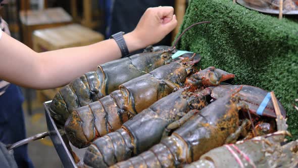 Man using arm to compare sizes fresh lobsters on street food market stall, Thailand