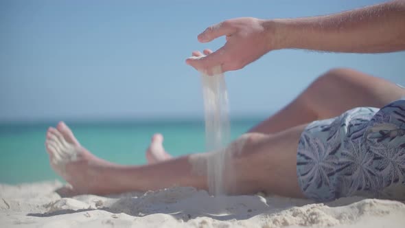 Guy Relaxing On Tropical Beach. Man Pouring Sand Through Fingers. Guy Sitting On Beach Caribbean.