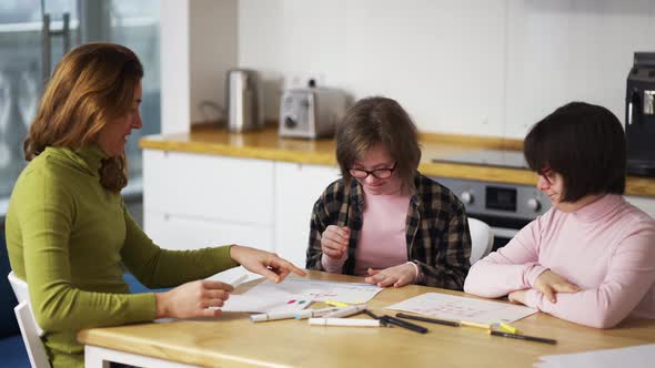 Two Girls with Down Syndrome Draw at the Kitchen Next to the Teacher or Mother