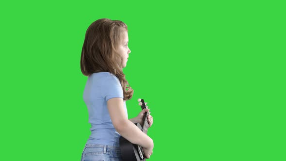 A Little Girl Walking with Ukulele in Hands on a Green Screen, Chroma Key