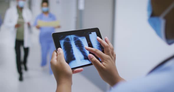 Mixed race doctor wearing face mask looking at x ray on tablet walking in hospital corridor