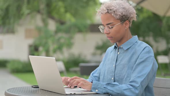 Young African Woman with Laptop Looking at Camera in Outdoor Cafe