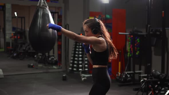 Female Boxer Performing Active Punching in Bandages Wearing Headphones