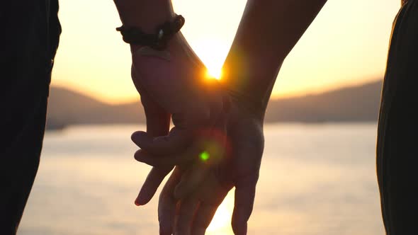 Male and Female Hands Holding Each Other at Sunset. Young Couple Standing on Seashore and Enjoying