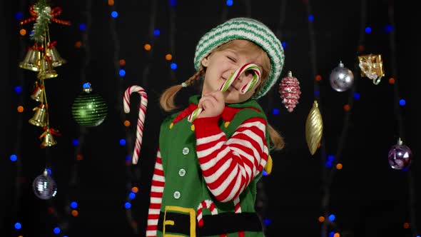 Kid Girl in Christmas Elf Santa Claus Helper Costume with Candy Cane Lollipop Joyful Smiling