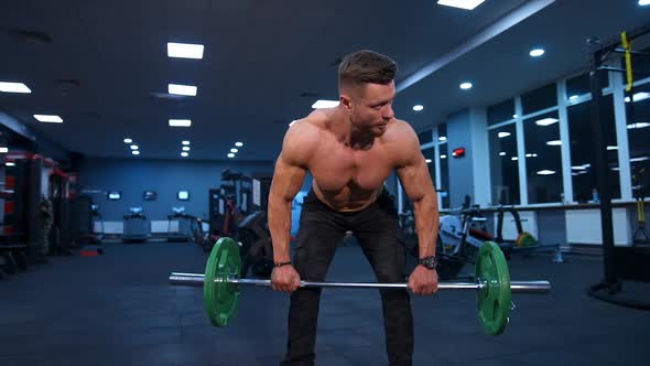 Male athlete trains with barbell in empty gym with modern equipment. Slow motion.