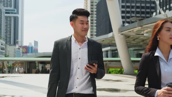 Asian young smart businessman using smartphone, walking outdoor to working office in city.