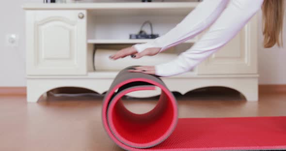 Young woman rolling red fitness or yoga mat before or after sports yoga practice