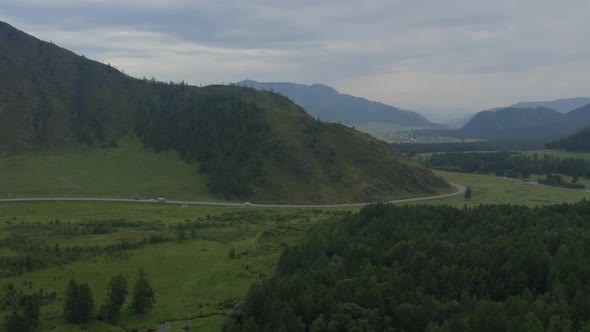 Traffic cars on road between field and mountains in Altai