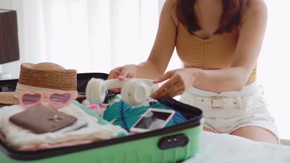 Young woman traveler sitting on the bed packing her suitcase preparing for travel