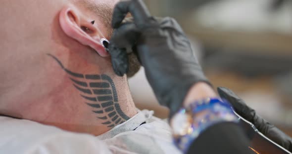 View From Behind of Neck and Head of Young Bearded Man with Tunnel Earring in Ear and Wing Tattoo on