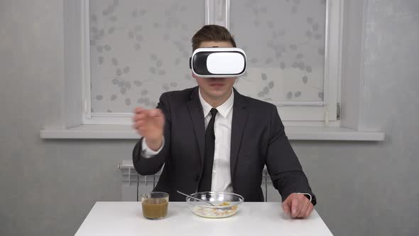 A Young Man in a Suit and a VR Helmet Eats Cereal and Drinks Coffee