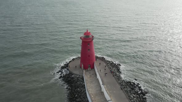 Tourists Walking Around The Poolberg Lighthouse With Ocean Waves Splashing On The Rocks At Dublin, I