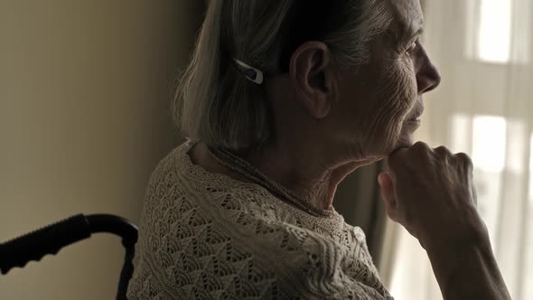 Senior Woman Sit on Wheelchair and Looks Through the Window