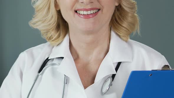 Experienced Physician with Stethoscope Holding Folder and Smiling Into Camera