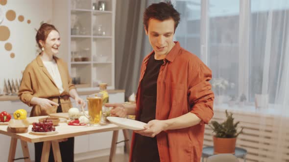 Joyous Family Couple Cooking Food and Setting Table for Dinner