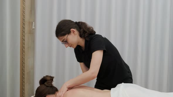 Female therapist massages a young woman on her back and shoulders. Relaxing massage.