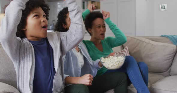 Mixed race lesbian couple and daughter watching tv eating popcorn high fiving