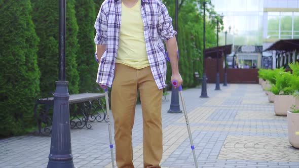 Stylish Man with an Injury on Crutches Walking in the Park on a Sunny Day Slow Mo