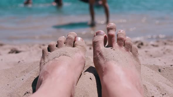 Tanned Red Bare Female Feet in Sand Lies on a Sandy Beach on Coast of the Ocean