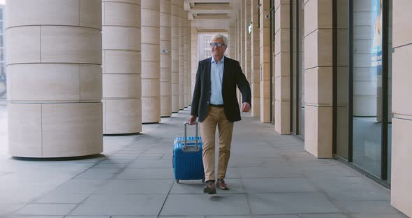 Slider Shot of Aged Businessman Walking Outside Modern Building with Luggage