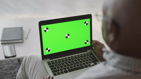 Over Shoulder View of Unrecognizable Senior African American Man Watching Tv Ion Laptop with Green