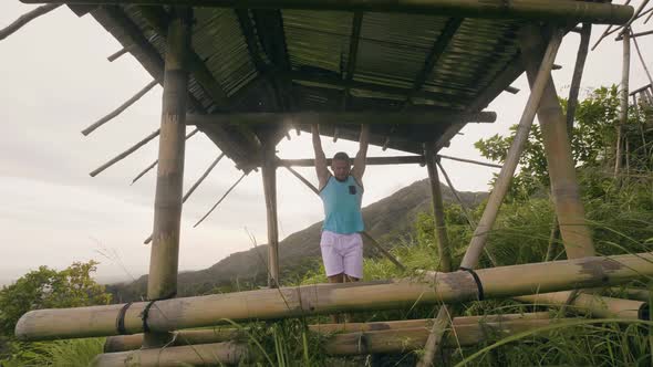 Sport Man Hanging on Wooden Crossbar Doing Abs Training on Tropical Nature Landscape. Fitness Man