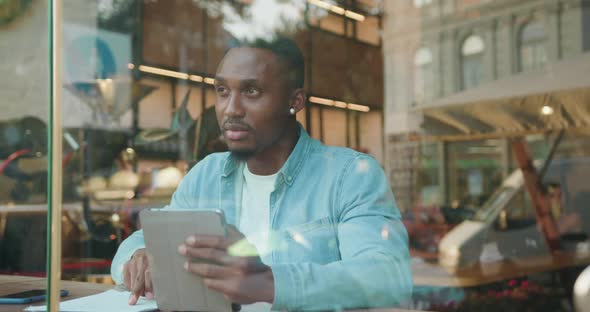 Black-Skinned Man Checking Documents with Datas from i-pad, Sitting in Cafe