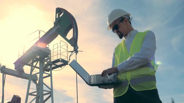 Sunlit Fuel Derrick and a Male Engineer Operating a Laptop in Front of It. Oil Industry, Petroleum