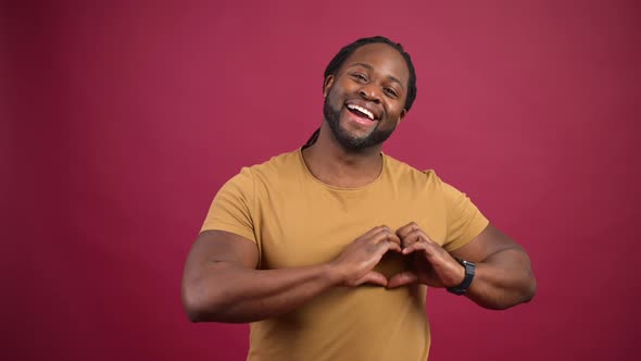 Cheerful AfricanAmerican Guy Shows Heart Shape Isolated on Red Background