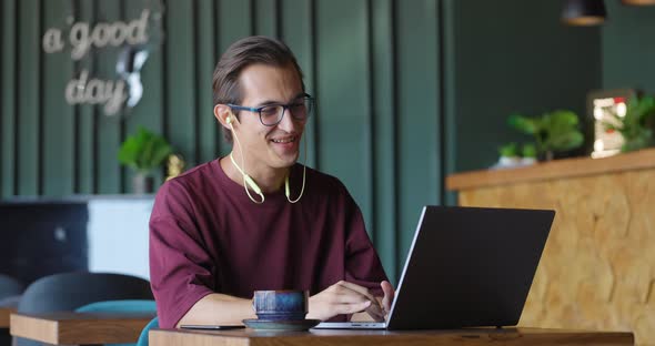 Young Man in Glasses Having a Video Call on Laptop While Sitting at a Cafe