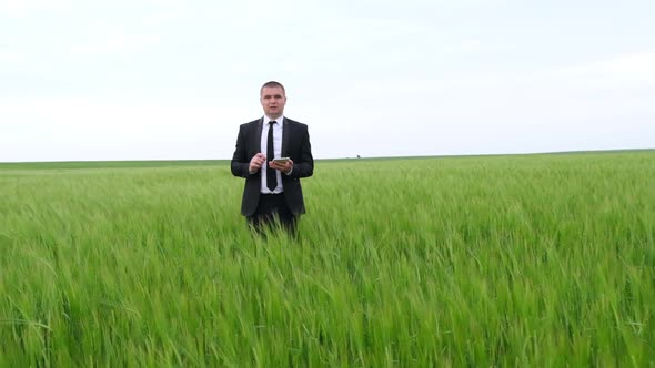 A Young Agronomist Holds a Tablet Computer with a Touchpad on a Green Wheat Field