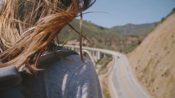 Close-up Back View Shot of Young Woman with Hair Flying in the Wind Enjoying View of Highway One at