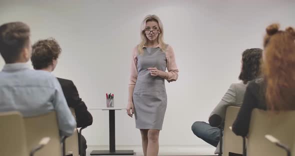 Confident Caucasian Adult Woman in Eyeglasses Standing in Front of Coworkers and Talking. Team