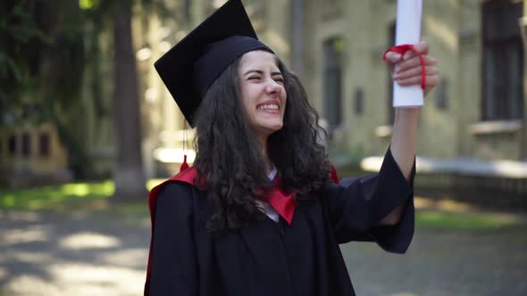 Excited Intelligent Beautiful Woman Kissing Diploma Standing at University Campus in the Morning