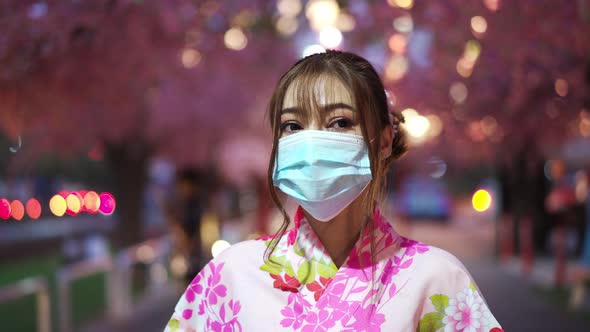 woman in yukata (kimono dress) wear a face mask and looking sakura flower or cherry blossom blooming