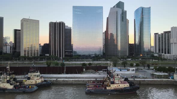 Aerial dolly left of boats in Puerto Madero docks near Paseo del Bajo highway and skyscrapers at sun