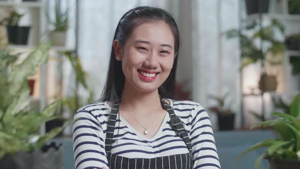 Close Up Of Asian Woman With Plants Crossing Her Arms And Smiling To Camera At Home