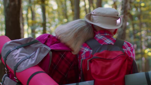 Grandmother Grandfather Senior Tourists Hikers Sitting on Tree and Hugging Kissing in Summer Wood