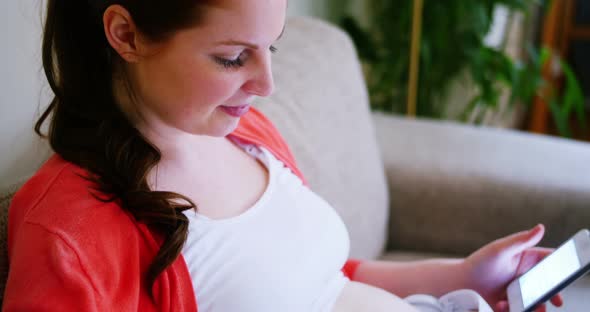 Pregnant woman placing headphones on stomach while using mobile phone