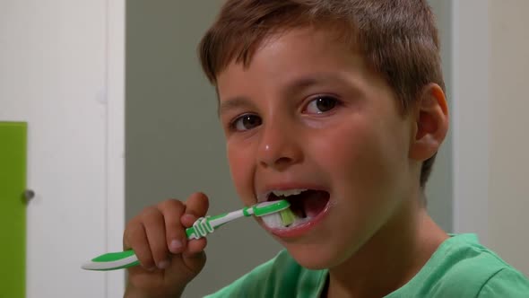 Closeup of the Little Tanned Boy Brushing His Teeth in the Bathroom