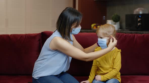 Mother Puts on Little Sick Daughter Protective Medical Mask at Home. Coronavirus Quarantine Lockdown