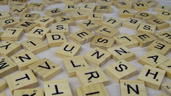 Letters scrabble scattered randomly on a white board. Camera travelling backward