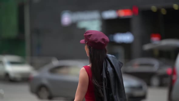 A Beautiful Female in a Cap and Red Dress, Holding a Leather Jacket in Her Hands, She Runs and Poses