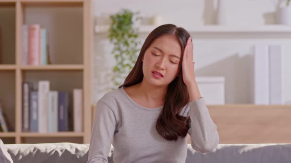 Asian woman sitting on sofa have a headache and Migraine feeling so stressed